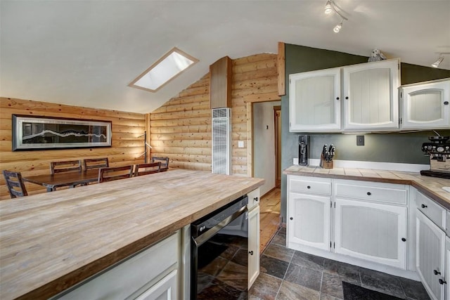 kitchen with tile counters, white cabinetry, rustic walls, and beverage cooler