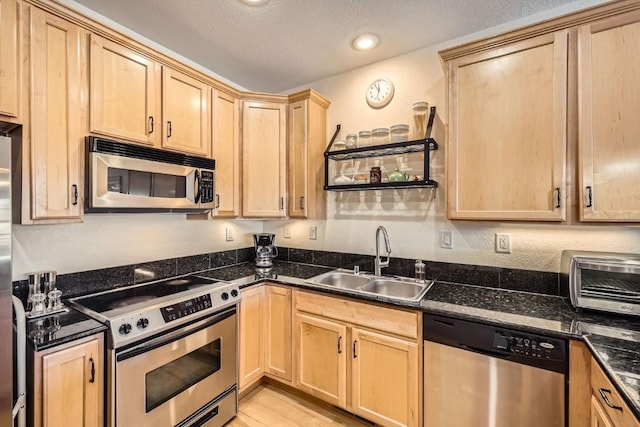 kitchen with a sink, light brown cabinetry, a toaster, light wood finished floors, and appliances with stainless steel finishes