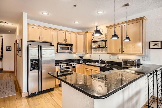 kitchen with light brown cabinets, a peninsula, appliances with stainless steel finishes, and a sink