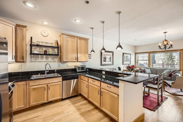 kitchen with light wood finished floors, stainless steel dishwasher, a sink, a peninsula, and open floor plan