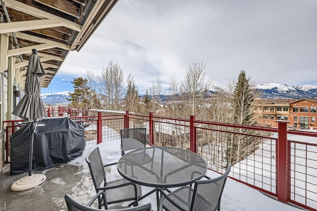 snow covered back of property with outdoor dining space, area for grilling, and a mountain view