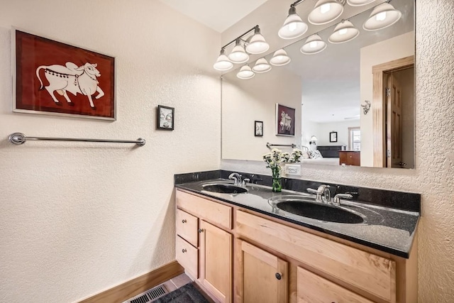 bathroom with a textured wall, visible vents, a sink, and double vanity