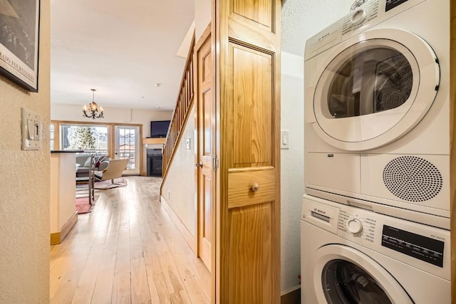 clothes washing area with laundry area, a textured wall, light wood-style flooring, stacked washer and dryer, and a notable chandelier