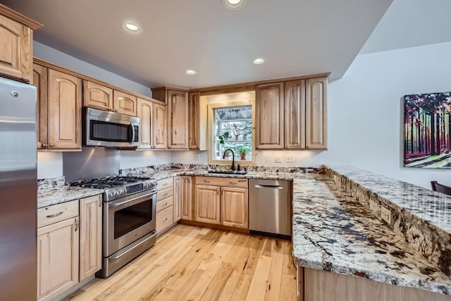 kitchen with light stone counters, a sink, light wood finished floors, stainless steel appliances, and a peninsula