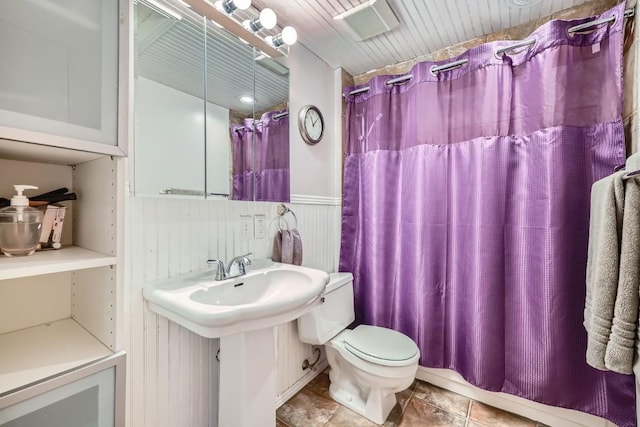 full bathroom featuring toilet, a shower with shower curtain, tile patterned flooring, and a wainscoted wall