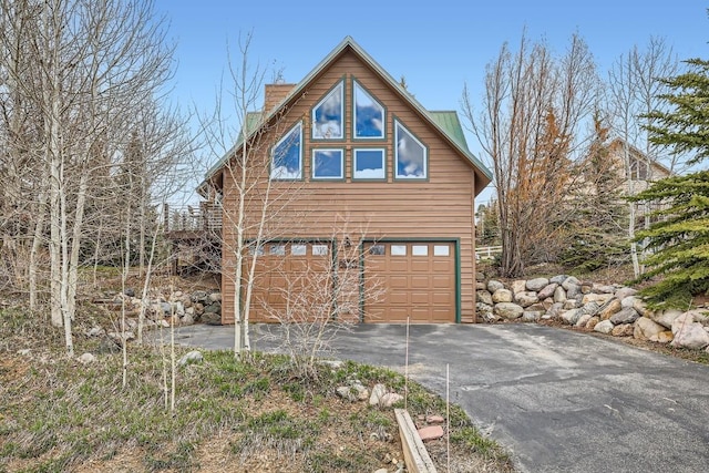 view of property exterior with an attached garage, a chimney, and driveway