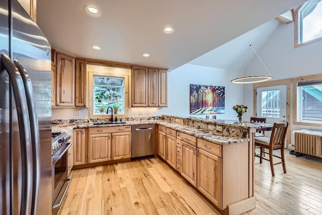 kitchen with a peninsula, light stone countertops, light wood-style floors, a sink, and stainless steel appliances