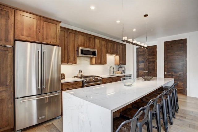 kitchen with light stone counters, a center island, a sink, high end appliances, and light wood-style flooring