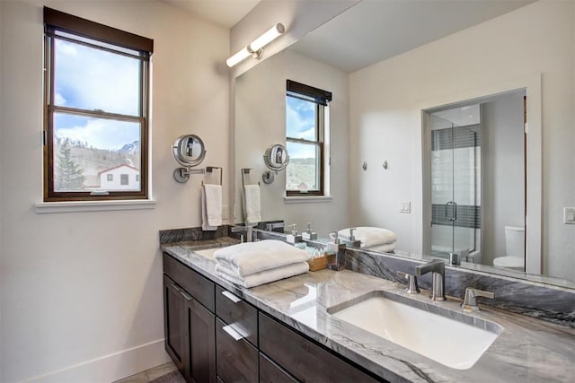 full bath with toilet, a sink, a stall shower, double vanity, and baseboards