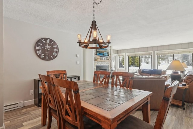 dining space featuring a baseboard heating unit, an inviting chandelier, light wood-style flooring, and a fireplace