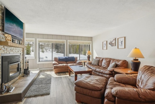 living room with a baseboard radiator, a textured ceiling, a stone fireplace, and wood finished floors