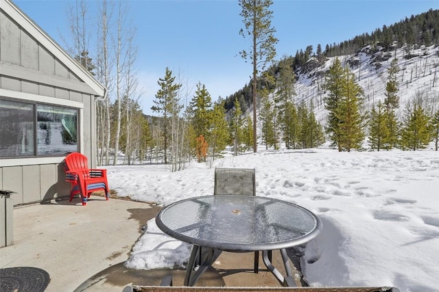 snow covered patio with outdoor dining space and a forest view