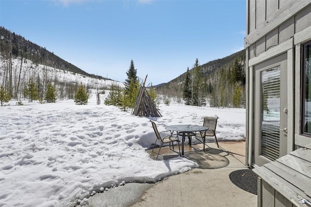 yard covered in snow featuring a mountain view and outdoor dining area