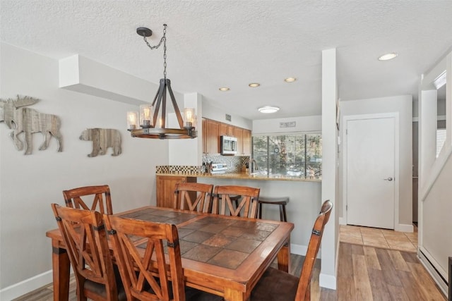 dining space with baseboards, light wood finished floors, an inviting chandelier, a textured ceiling, and a baseboard heating unit