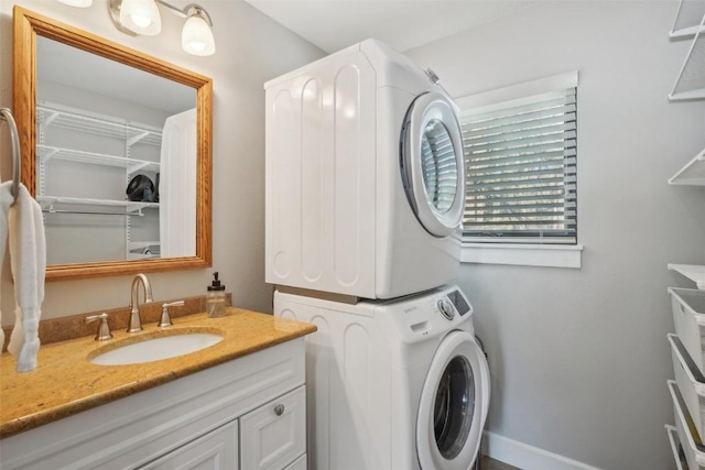 washroom featuring laundry area, baseboards, stacked washer / drying machine, and a sink