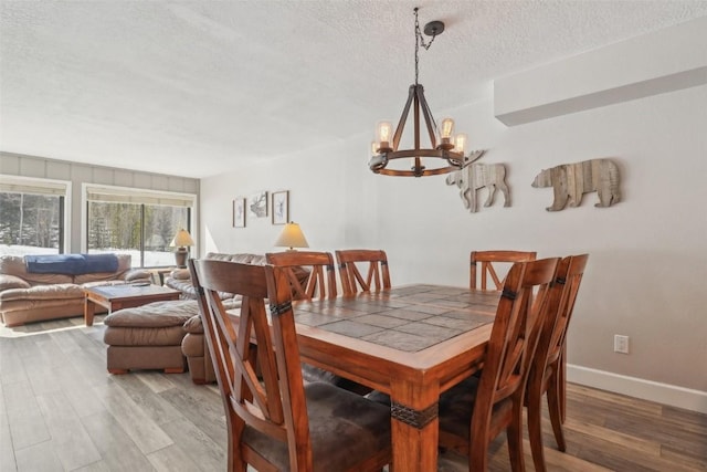 dining area featuring baseboards, a textured ceiling, light wood-type flooring, and an inviting chandelier