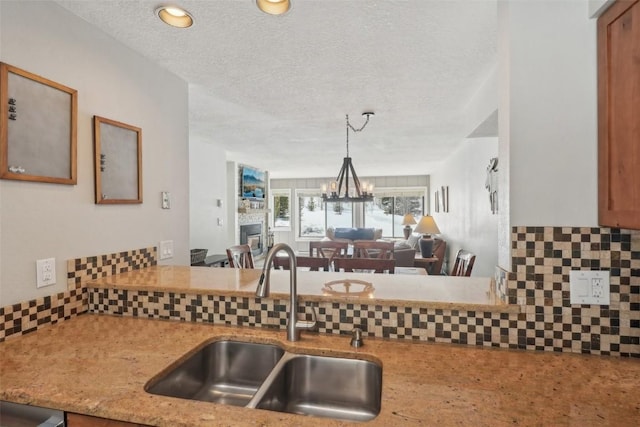 kitchen featuring tasteful backsplash, a fireplace, an inviting chandelier, a textured ceiling, and a sink