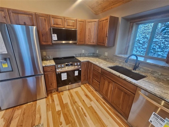 kitchen with light stone countertops, appliances with stainless steel finishes, vaulted ceiling, a sink, and light wood-type flooring
