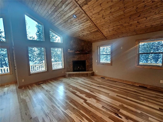 unfurnished living room with wooden ceiling, wood finished floors, a stone fireplace, and high vaulted ceiling