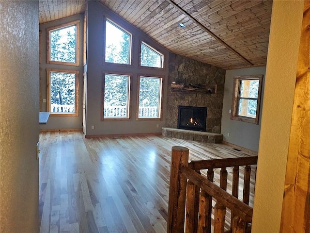 unfurnished living room with wooden ceiling, wood finished floors, a stone fireplace, and plenty of natural light