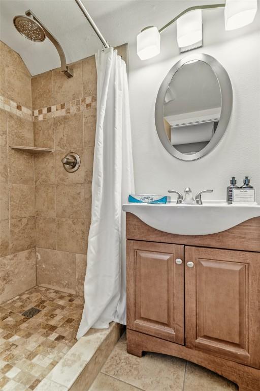 bathroom featuring tile patterned flooring, a tile shower, and vanity
