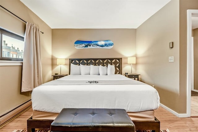 bedroom featuring light wood finished floors, baseboards, and a baseboard radiator
