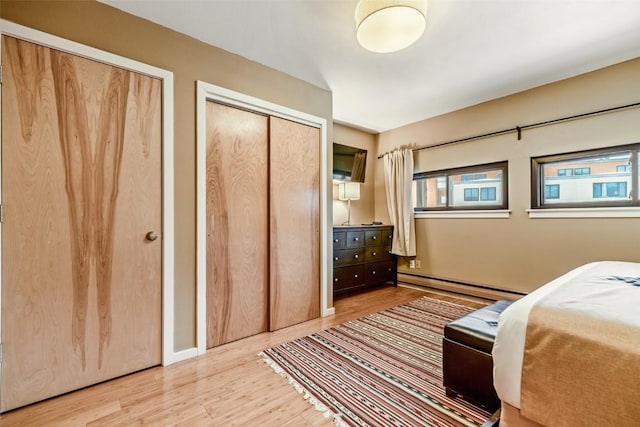 bedroom with a baseboard heating unit, wood finished floors, and two closets