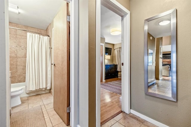 full bath with shower / bath combo, toilet, tile patterned flooring, and baseboards