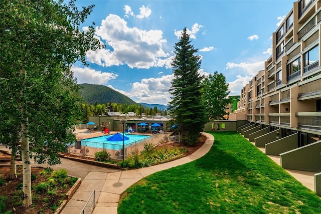 community pool with fence, a yard, and a mountain view