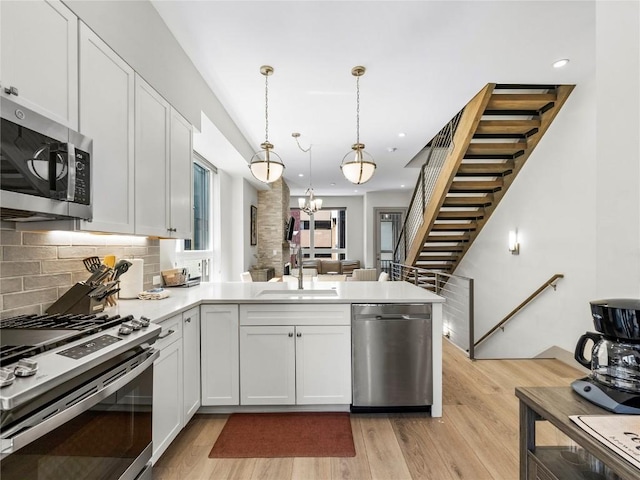 62 W 3rd St Unit D, Silverthorne, CO 80498 - kitchen with stainless steel appliances, a chandelier, a peninsula, light wood-style floors, and white cabinetry