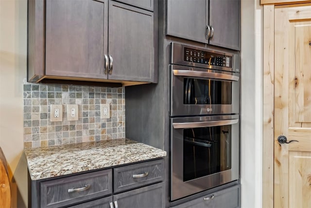 kitchen with light stone countertops, stainless steel double oven, and backsplash