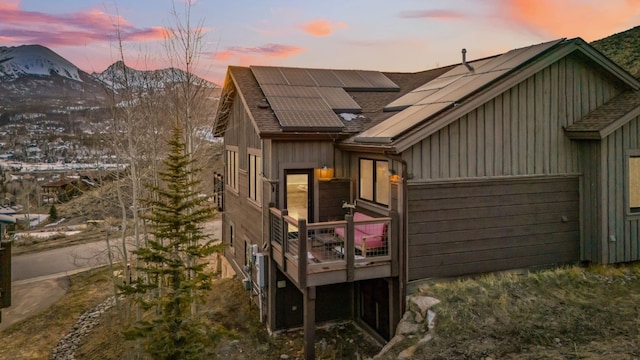 back of property with roof with shingles, a garage, roof mounted solar panels, a deck with mountain view, and board and batten siding