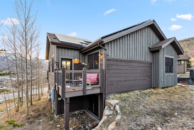 exterior space featuring board and batten siding, roof mounted solar panels, and a deck
