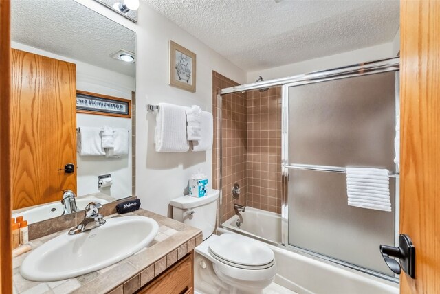 bathroom featuring toilet, vanity, a textured ceiling, and combined bath / shower with glass door