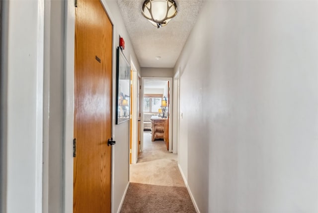 hallway featuring light carpet, a textured ceiling, and baseboards