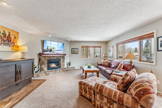 carpeted living room featuring baseboards, a stone fireplace, a textured ceiling, and rail lighting