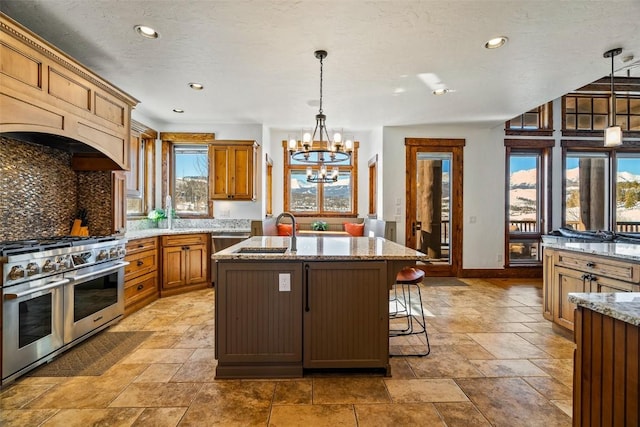 kitchen with pendant lighting, double oven range, sink, a chandelier, and a center island with sink