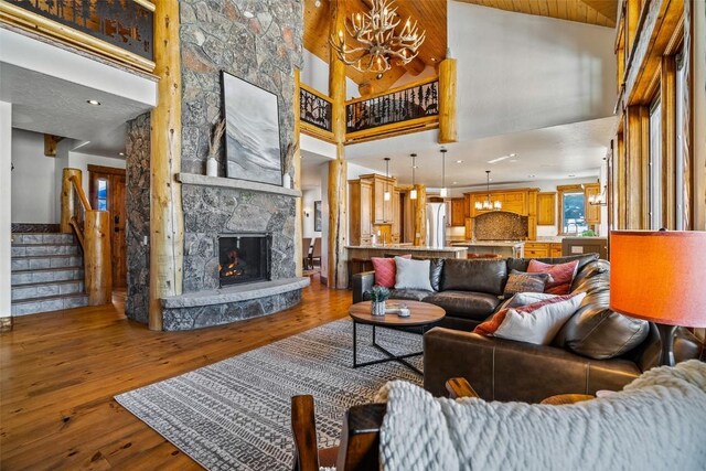 living room featuring a high ceiling, hardwood / wood-style floors, a chandelier, and a stone fireplace