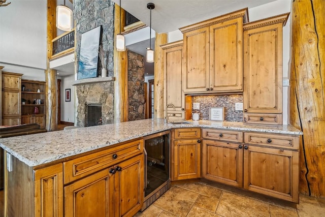 kitchen featuring a stone fireplace, tasteful backsplash, wine cooler, hanging light fixtures, and kitchen peninsula