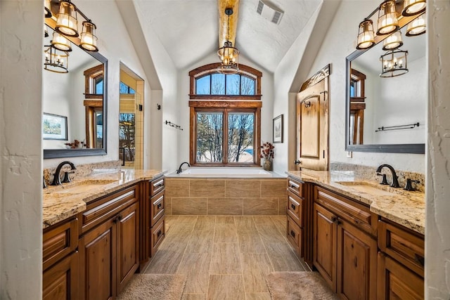 bathroom featuring tiled bath, vanity, lofted ceiling, and a chandelier