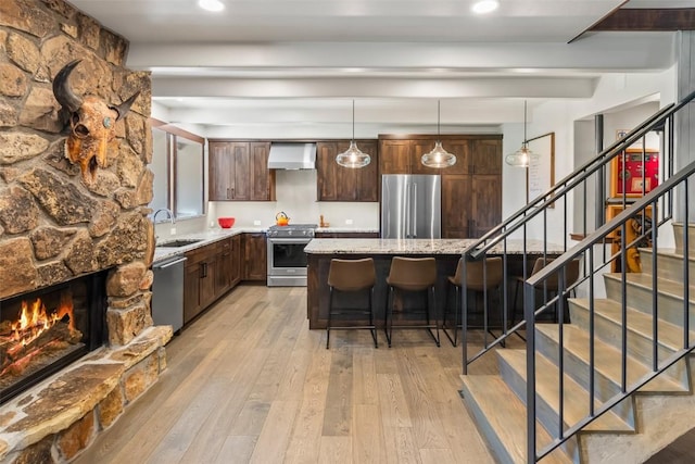 44 Maverick Way, Silverthorne, CO 80498 - kitchen featuring stainless steel appliances, a sink, wall chimney range hood, light wood finished floors, and a breakfast bar area