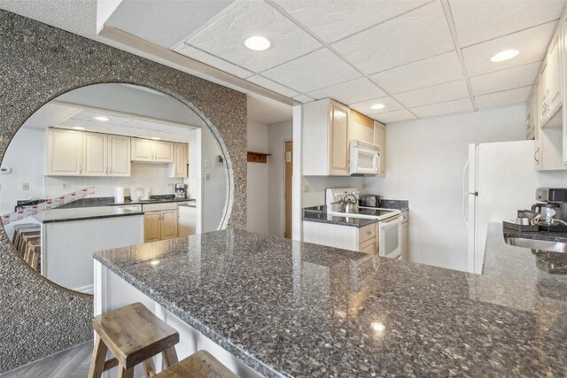 kitchen featuring a peninsula, a breakfast bar area, a sink, and white appliances