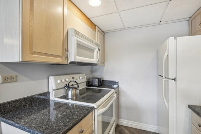 kitchen with baseboards, white appliances, dark stone countertops, and a drop ceiling