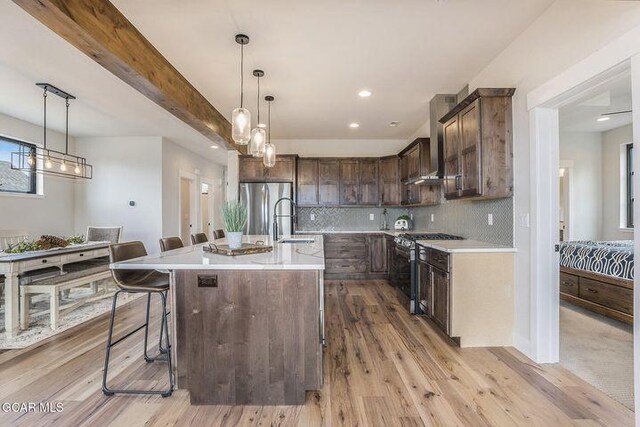 kitchen featuring dark brown cabinetry, light countertops, wall chimney exhaust hood, a sink, and stainless steel appliances