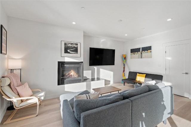 living room with recessed lighting, a glass covered fireplace, and light wood-style flooring