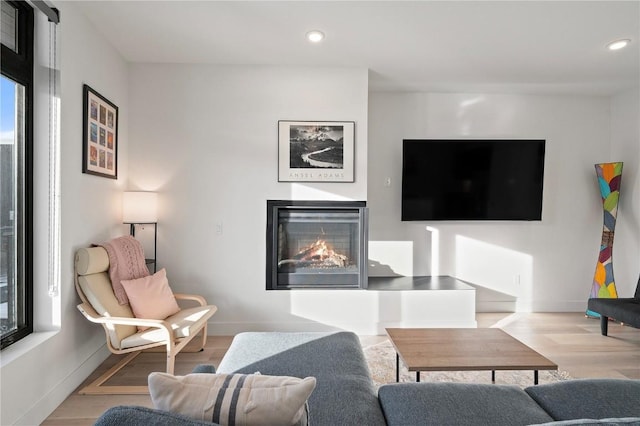 living area featuring baseboards, a glass covered fireplace, wood finished floors, and recessed lighting