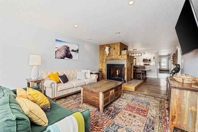 living area with a warm lit fireplace, wood finished floors, a textured ceiling, and recessed lighting