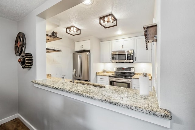 kitchen featuring light stone counters, stainless steel appliances, a sink, a textured ceiling, and white cabinetry
