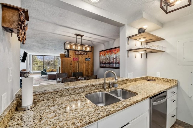 kitchen featuring stainless steel dishwasher, a sink, light stone countertops, a textured ceiling, and white cabinetry