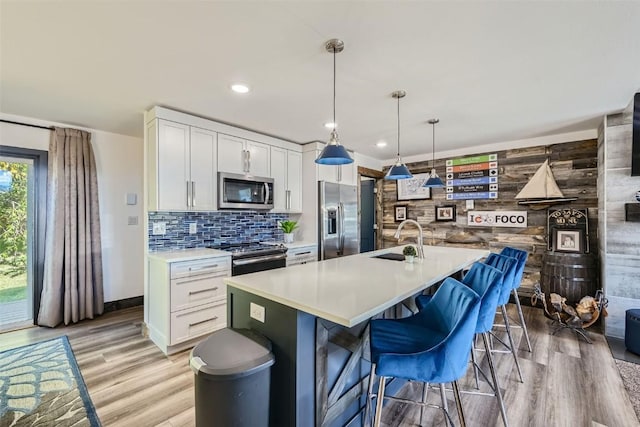 kitchen with stainless steel appliances, a sink, light wood-type flooring, white cabinetry, and light countertops